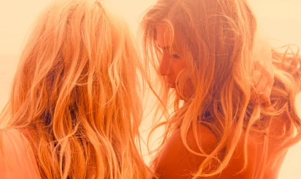 Close-up portrait of two blond women with long wavy hair bathed in warm orange sunset light by Stephanie Vovas