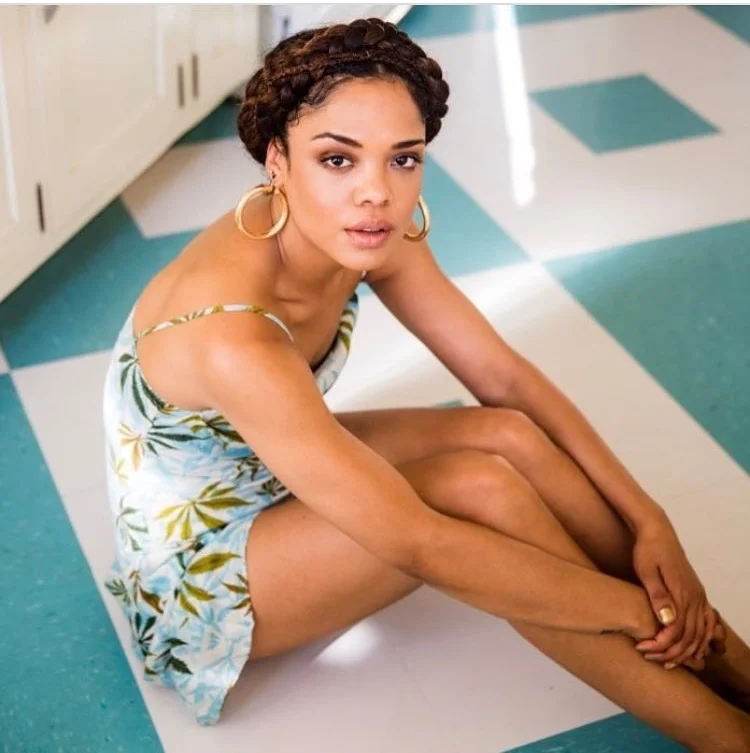 Tessa Thompson, a young African-American woman, sits cross-legged on a blue and white checkered floor, looking directly at the camera.