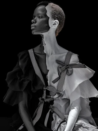 Monochrome fashion portrait of a woman with striking makeup and a two-tone ruffle dress against a dark backdrop, artistic and dramatic.