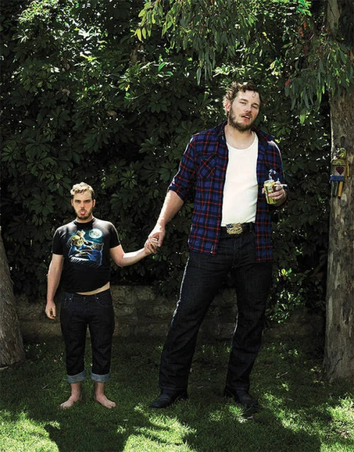 A playful image of two men, one notably taller, holding hands in a lush backyard setting, under the shade of leafy trees.