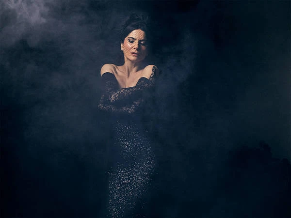Elegant woman in black dress and lace gloves posing in a smoky, dark environment for a fashion or beauty portrait.