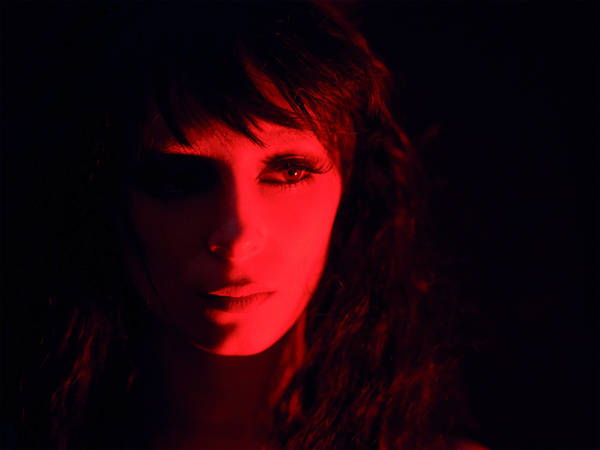 Close-up portrait of a woman bathed in deep red light, featuring dark hair and dramatic shadows in a moody studio setting.