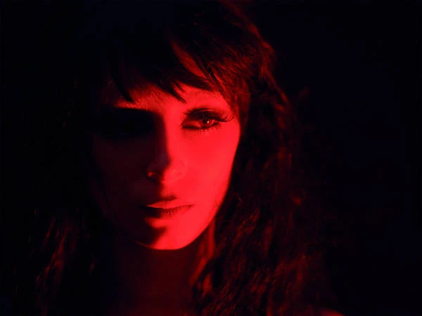 Close-up portrait of a woman bathed in deep red light, featuring dark hair and dramatic shadows in a moody studio setting.