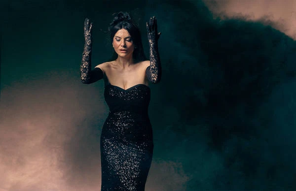 Elegant woman in black gown and lace gloves poses in a dramatic portrait with soft, colorful background. Fashion or beauty concept.