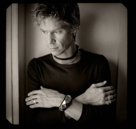 Portrait of a man with arms crossed wearing a dark top, choker necklace, and a studded cuff bracelet, photographed by Joseph Cultice.
