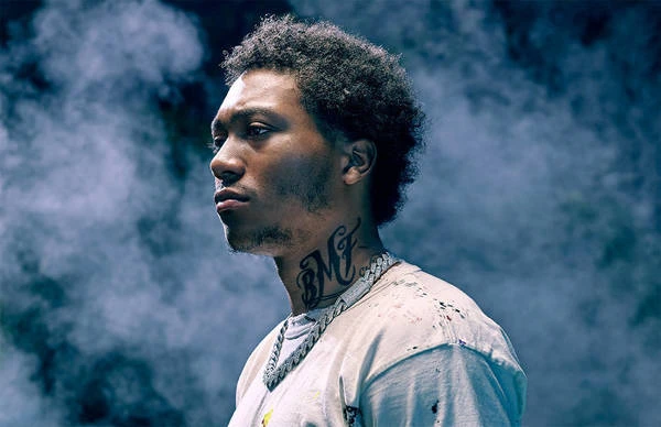 Portrait of a young adult man in a white tee shirt with smoke in the background, wearing an iced out chain necklace.