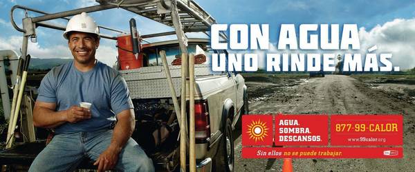 Construction worker wearing a hardhat and blue shirt sits on the back of a pick-up truck next to a dirt road on a sunny day.