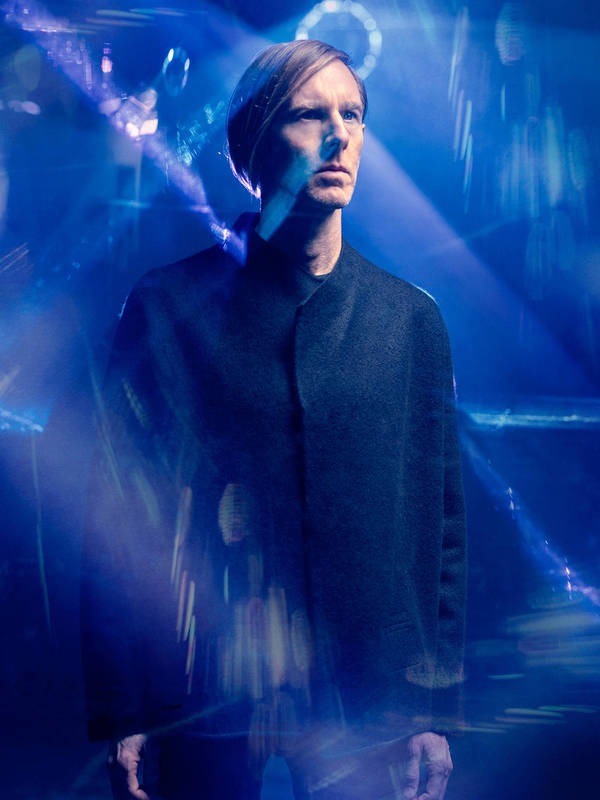 Portrait of a man with blond hair wearing a dark jacket against a blue and light blue bokeh background. Moody, artistic lighting.