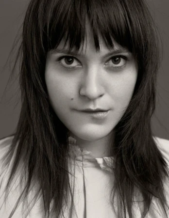 Close-up portrait of a woman with dark hair and bangs biting her lower lip, photographed by Joseph Cultice.