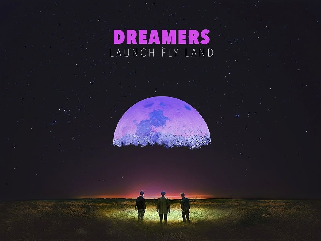 Three people standing in a field at night beneath a large moon or planet with the text DREAMERS LAUNCH FLY LAND.