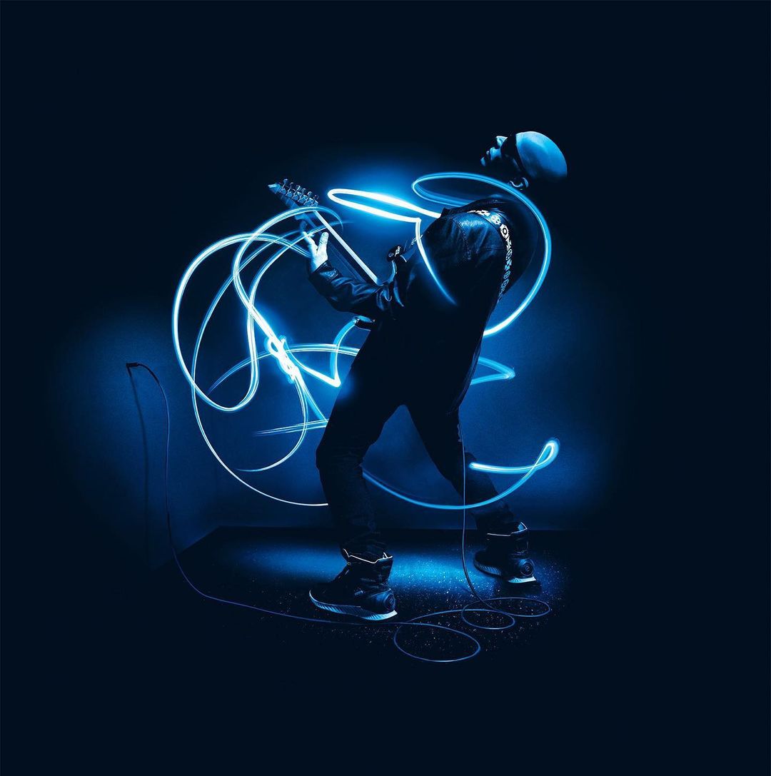 Musician in silhouette playing an electric guitar with blue light trails on a dark blue background.