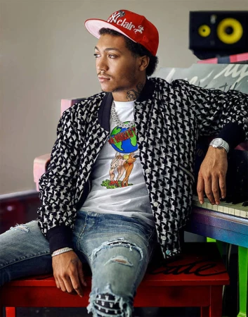 Young man wearing a red baseball cap and printed bomber jacket sitting by a colorful piano, photographed by Joseph Cultice.
