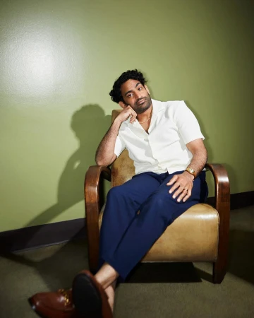 Man in a white shirt and blue trousers seated in a leather armchair against a green wall