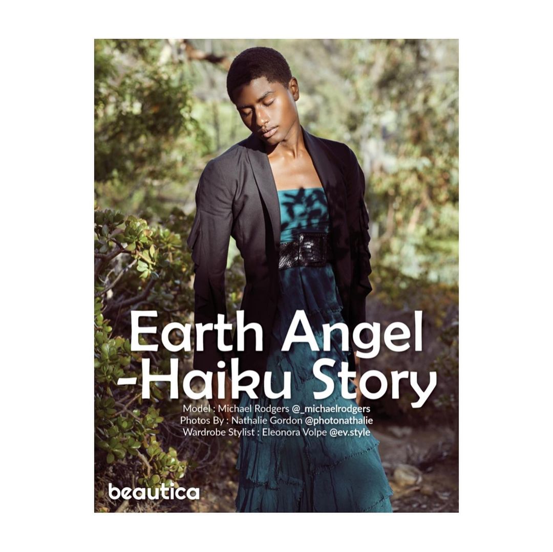 Black man wearing a black blazer and teal dress standing outdoors among greenery, photographed by Nathalie Gordon