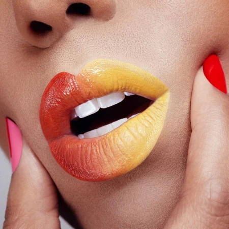 Close-up of lips with gradient red and yellow lipstick and fingers holding cheeks by photographer Nathalie Gordon.