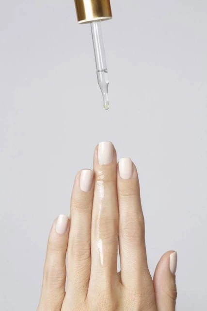 Close-up of serum or oil dropping from a glass dropper onto a woman's hand, against a neutral background. Beauty and wellness.