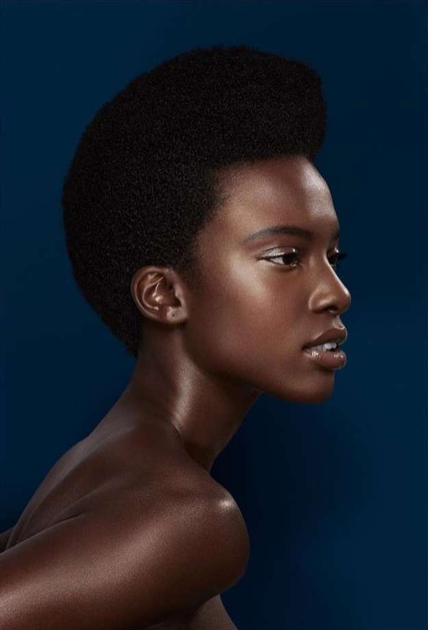 Portrait of a dark-skinned woman in a beauty shot against a solid dark blue background. The focus is on her hairstyle and complexion.