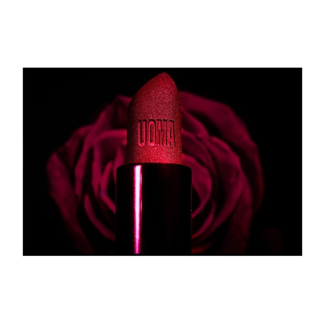 Close-up of a red UOMA Beauty lipstick against a blurred background of a dark red rose, product photography for beauty industry.