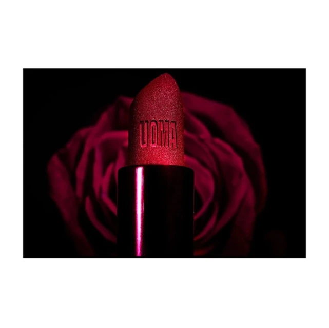 Close-up of a red UOMA Beauty lipstick against a blurred background of a dark red rose, product photography for beauty industry.