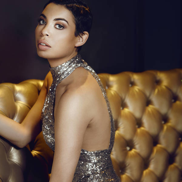 Adult woman poses in a photo studio with neutral background and strobe lighting for fashion and beauty photography, wearing an elegant top.