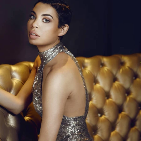 Adult woman poses in a photo studio with neutral background and strobe lighting for fashion and beauty photography, wearing an elegant top.