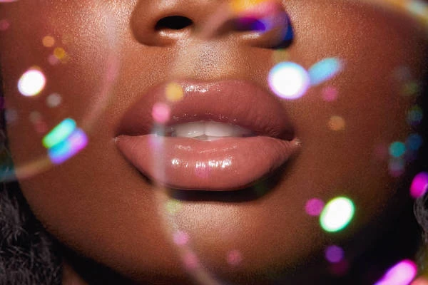 Close-up of a Black woman's face featuring glossy lips, soft skin texture, and colorful bokeh lights creating a glamourous, diffused effect.