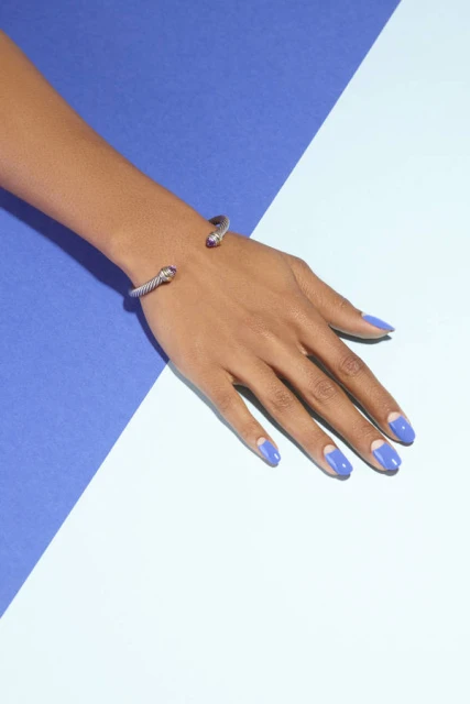 Close-up of a woman's hand with blue nails wearing a silver bracelet against a blue and light blue background.