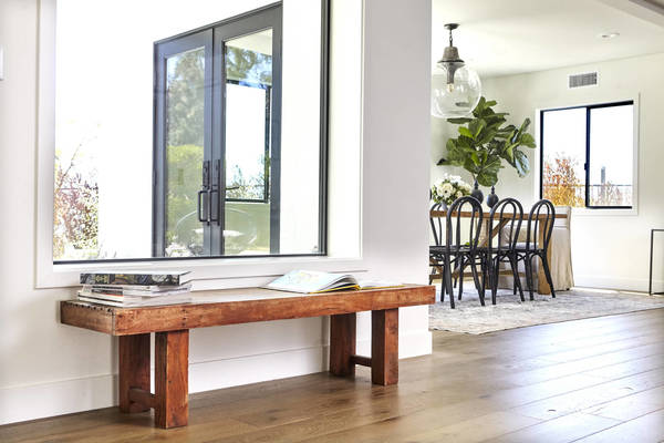 Bright interior shot of a modern foyer featuring a wooden bench with books, a view through the window to an outdoor scene, and a dining area.