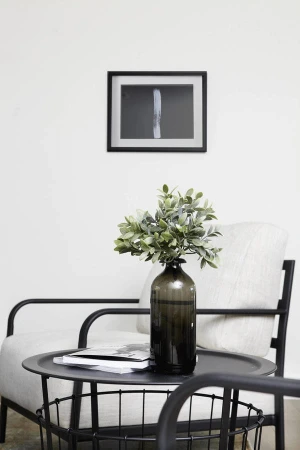 Interior design featuring a leafy plant in a bottle vase on a black metal table next to a modern armchair and framed art print.