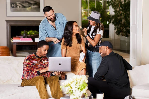 On-set scene featuring five people including a woman having her makeup done, two people working on computers and a hair stylist.