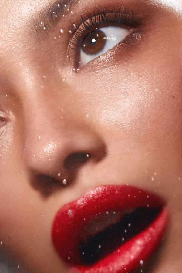 Close-up portrait of a woman with bold red lips and delicate water droplets scattered across her face.