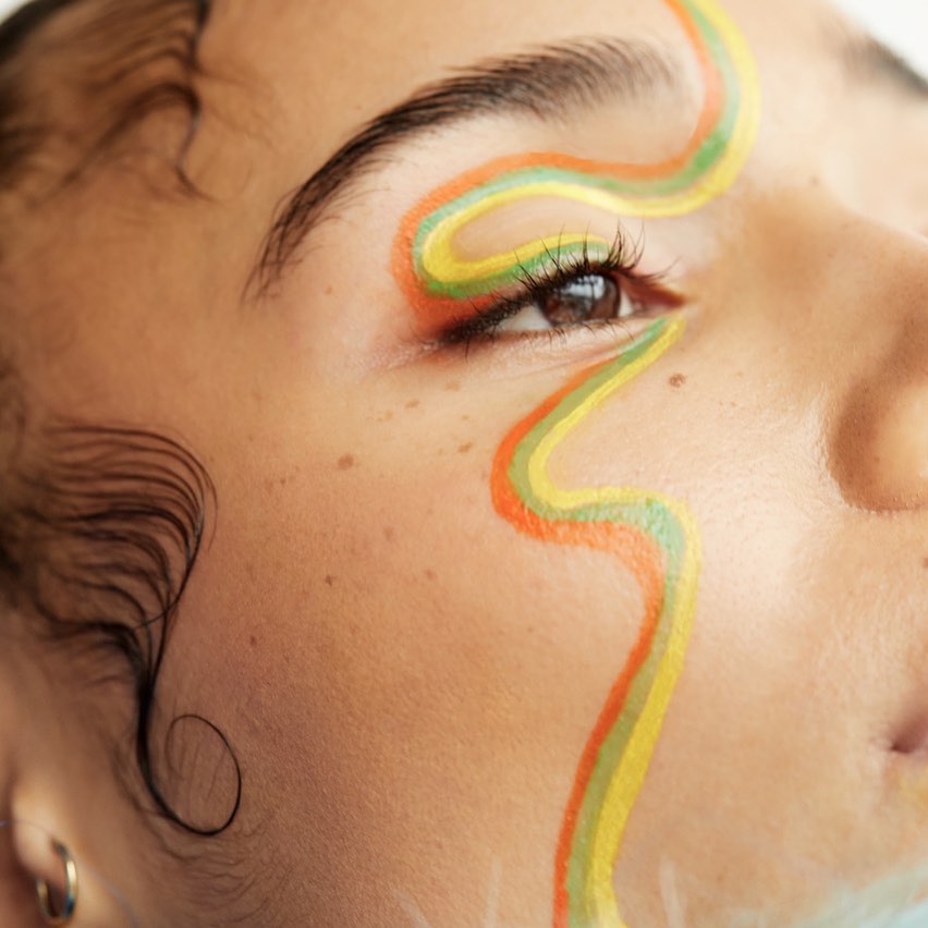 Close-up portrait of a person with colorful wavy face paint across their eye and cheek by photographer Nathalie Gordon.