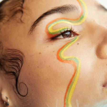 Close-up portrait of a person with colorful wavy face paint across their eye and cheek by photographer Nathalie Gordon.
