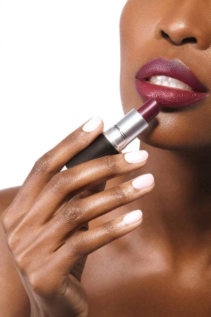 Close-up of dark-skinned woman applying deep plum lipstick with manicured nails against white background, beauty and cosmetics.