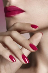 Close-up portrait of a woman with vibrant magenta lipstick and matching glossy manicured fingernails near her face.