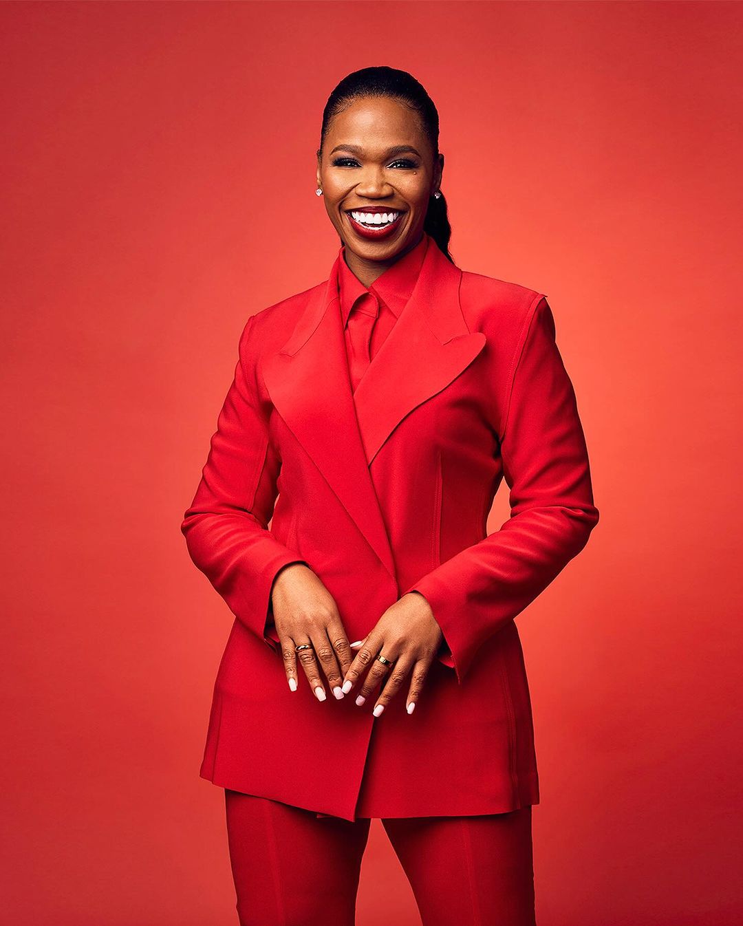 Portrait of a smiling African-American woman in a red pantsuit against a red background, looking directly at the camera.