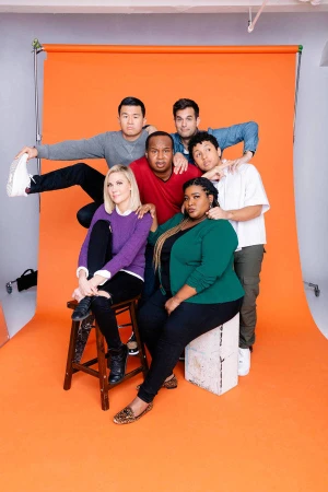 Group photo of six adults in casual clothing in a photo studio with an orange backdrop, posing and smiling at the camera.