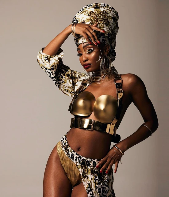 Glamorous woman in gold and leopard print outfit with a matching headwrap, posing confidently in a studio. Beauty and fashion shot.