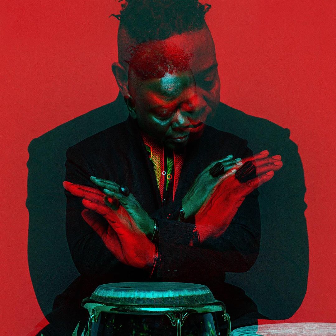 Portrait of a Black male musician seated behind a conga drum, with a green and red color shift and red background.