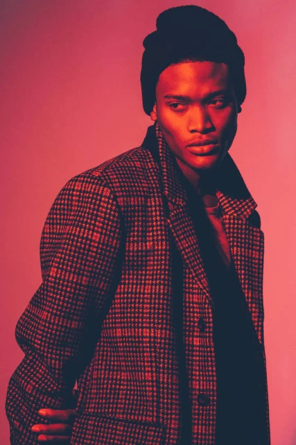 Portrait of a handsome adult male of African descent wearing a beanie hat and a red and black checkered overcoat in a photo studio.
