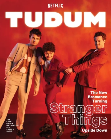 Netflix's TUDUM promotional cover with three young men in suits and shiny black shoes posing against a vibrant gradient orange backdrop.