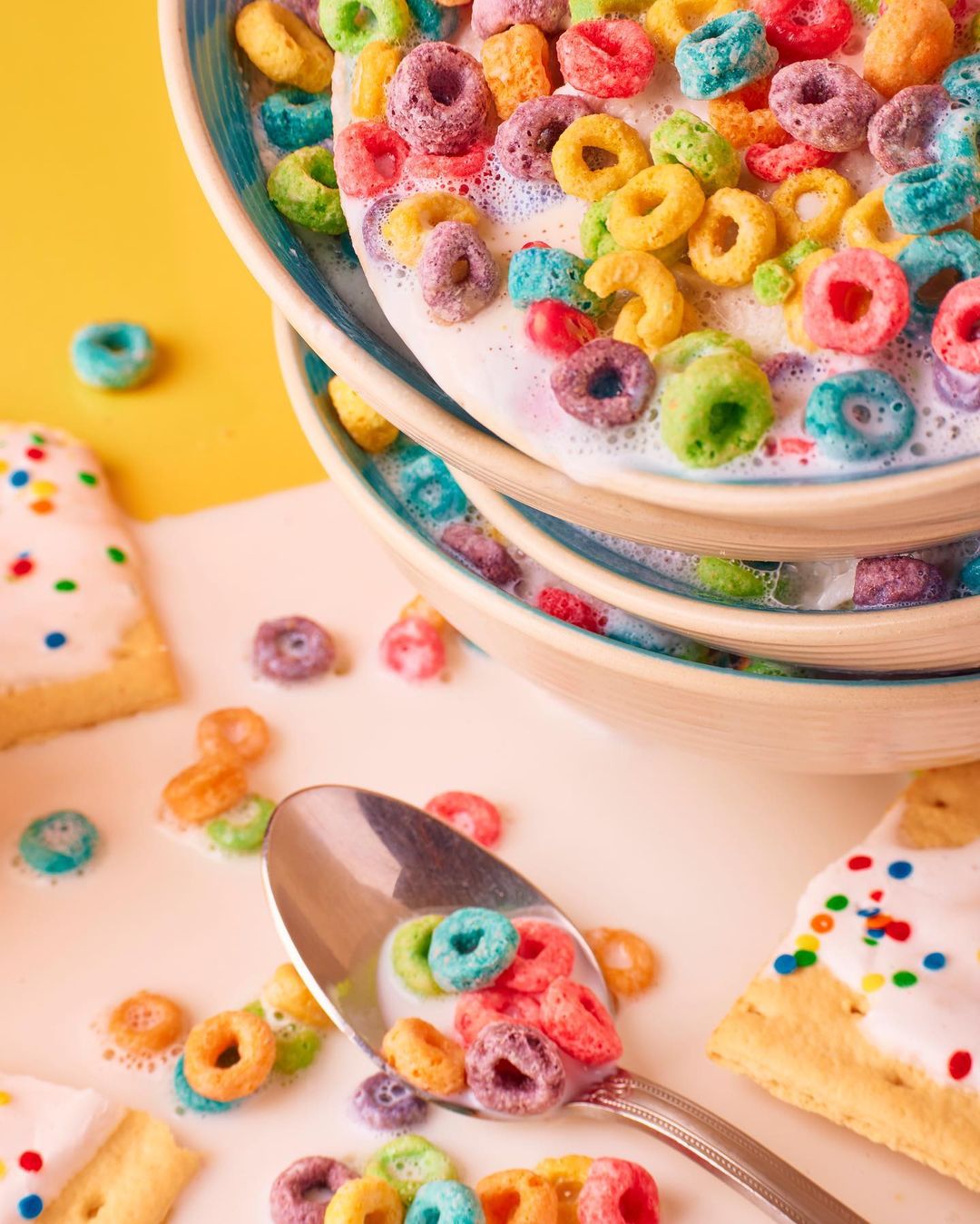 Stacked bowls of colorful loop cereal in milk, featuring a spoon with cereal and frosted sugar cookies; bright, cheerful food photography.