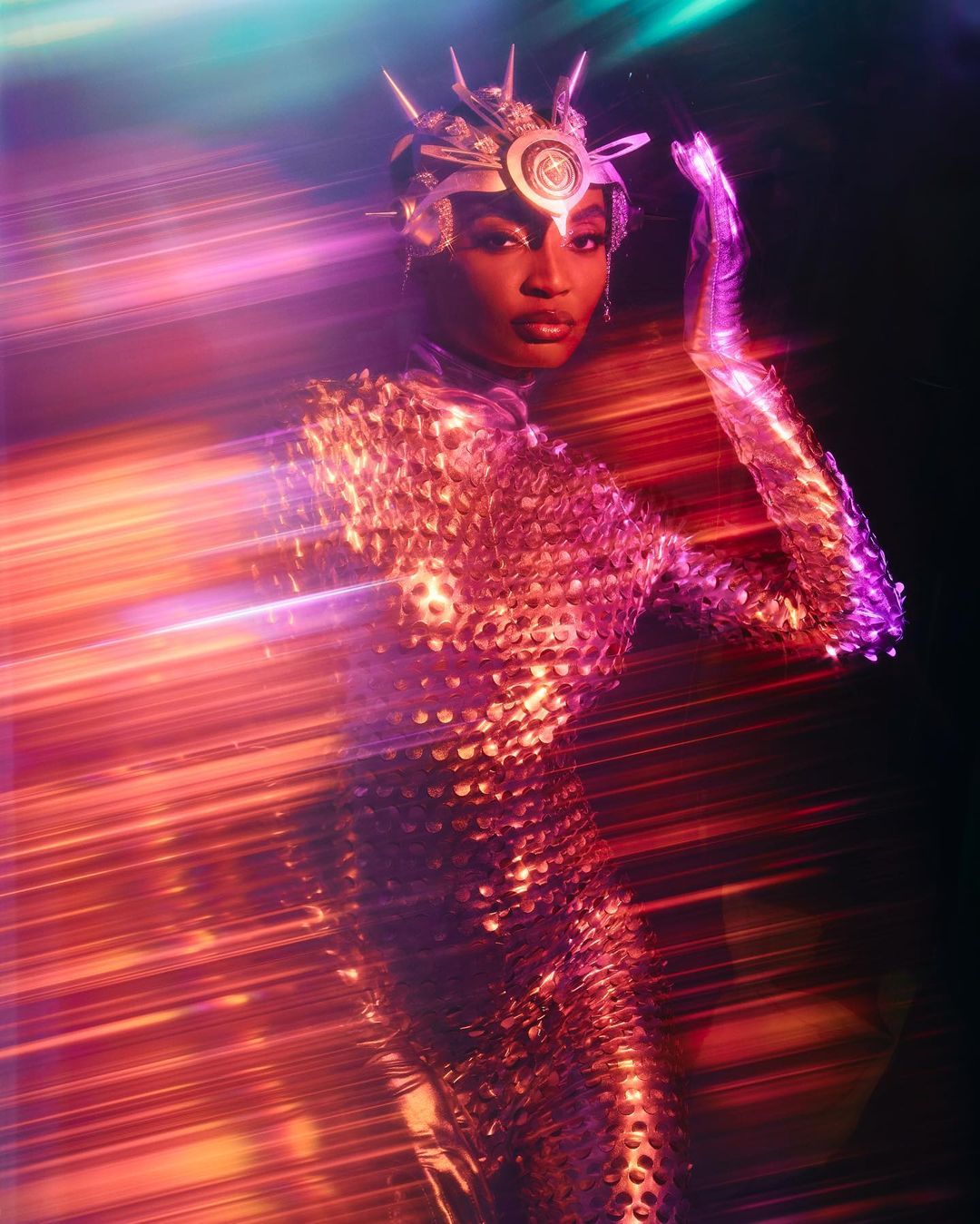 Portrait of a woman in a metallic dress and crown posing in front of a red and blue light trail in a studio. Fashion and beauty shot.
