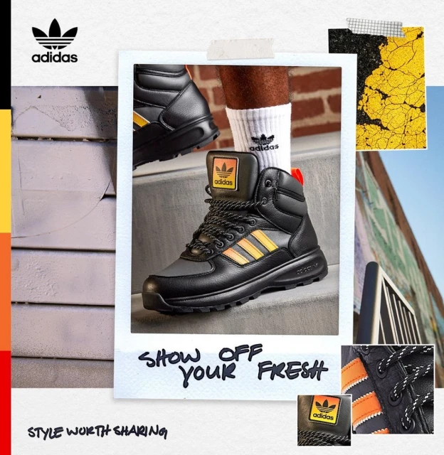 Stylish black leather Adidas boots with orange stripes and white socks on a concrete step, displayed in a studio setting with branding.