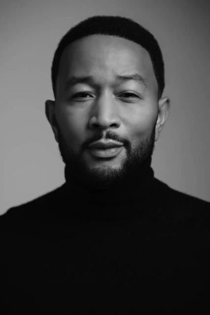Portrait of a black adult male in a blue jacket and white collared shirt against a solid blue background in a photo studio.