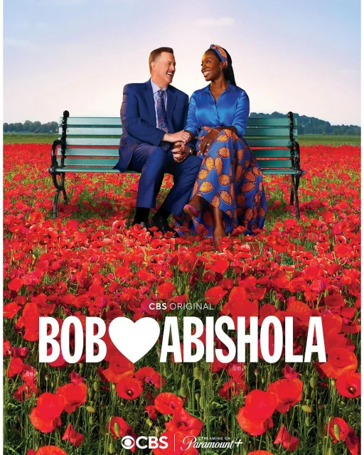 Bob Hearts Abishola cast sitting on a park bench in a field of red flowers; comedy series promotion; outdoor setting.