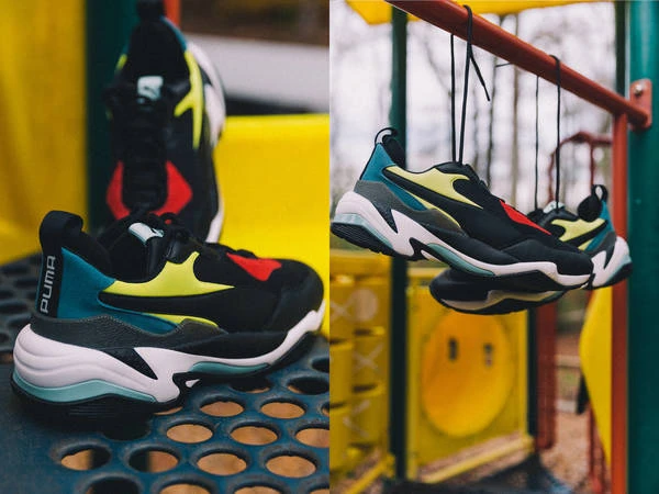 Eye-level outdoor shot of Puma Thunder sneakers in black, teal, yellow, and red; hanging from a bar and displayed on a perforated surface.