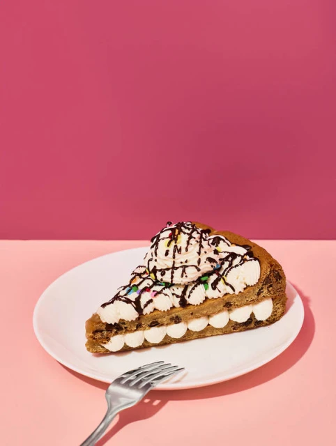 Delicious-looking dessert slice on a white plate with a fork, set against a split pink background, food photography, sweets.