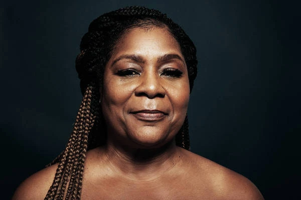Close-up portrait of a smiling Black woman with braided hair against a dark backdrop, showcasing beauty and photographic technique.