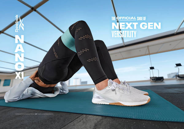 Fitness ad for Reebok Nano X1 shoes featuring woman in athletic wear exercising on mat against urban backdrop on rooftop.